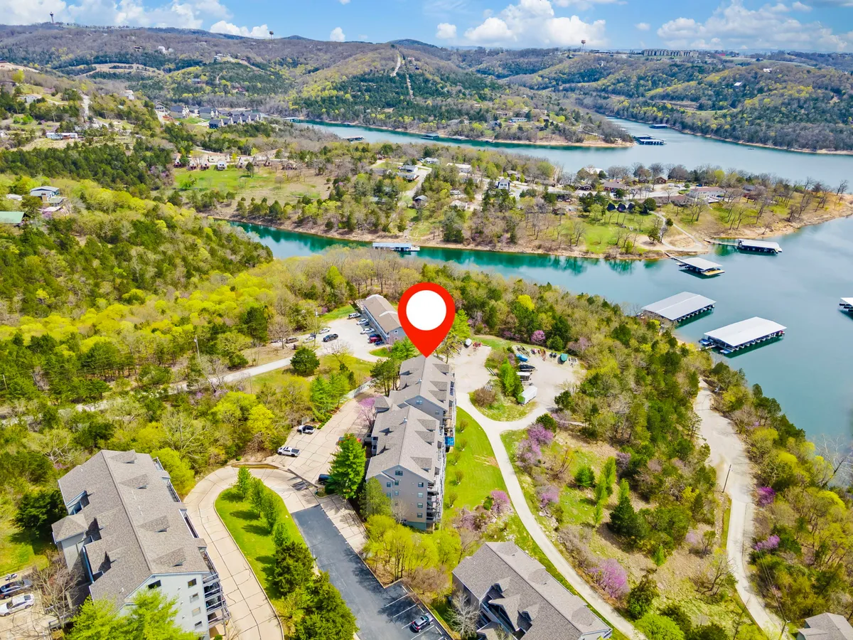 A picturesque view of Table Rock Lake framed by shorefront greenery and nearby buildings, with activities such as boating and walking along the shore in evidence. The natural setting glows under soft light, evoking a sense of lakeside relaxation and outdoor adventure.
