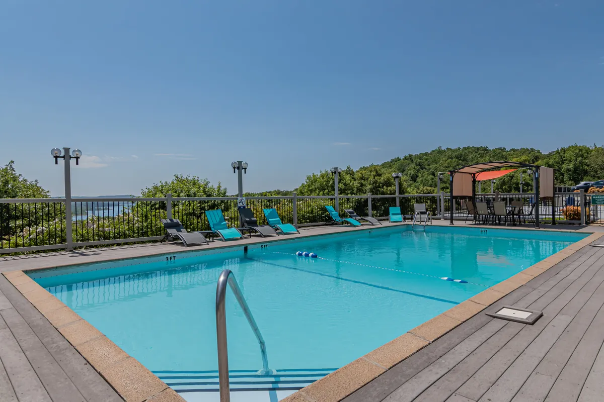 This image features a sparkling outdoor swimming pool surrounded by comfortable lounge chairs and a shaded canopy area, with lush landscaped greenery providing a serene backdrop. The tranquil setting conveys a leisurely resort atmosphere and hints at the social and relaxing opportunities available poolside.