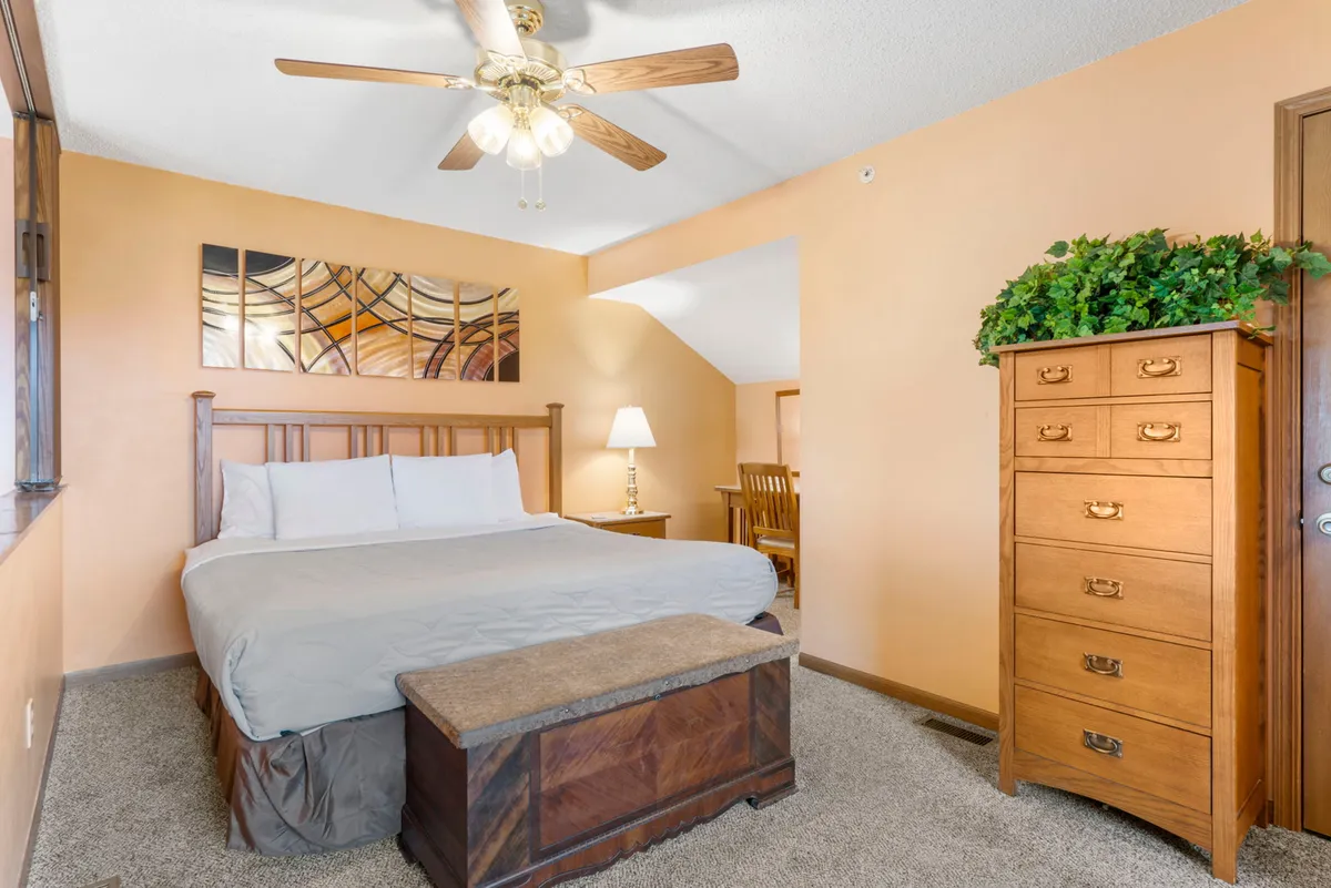 A welcoming bedroom featuring a comfortable bed, decorative artwork above the headboard, a nightstand, and a chest of drawers. The space exudes warmth and comfort for a restful night.