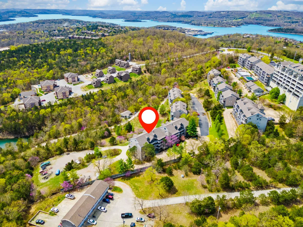An elevated view of the property showing clustered condo buildings, a spacious parking area, lush trees, and the shimmering nearby water. The image conveys a sense of privacy for each unit within a vibrant, scenic environment, ideal for families seeking both togetherness and retreat.