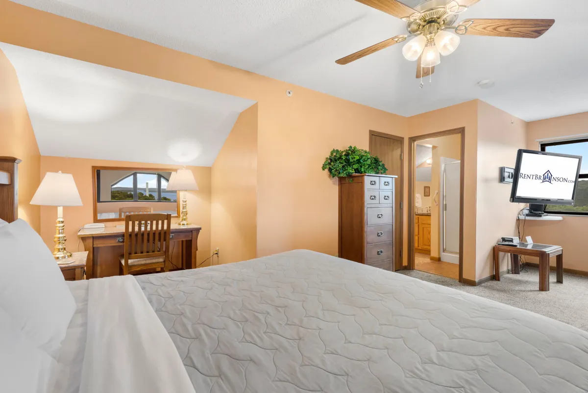 A loft-like bedroom with a bed, desk, dresser, television, and a window allowing in natural light. The space is functional yet cozy, with a layout that could easily serve multi-generational families or couples needing extra privacy.