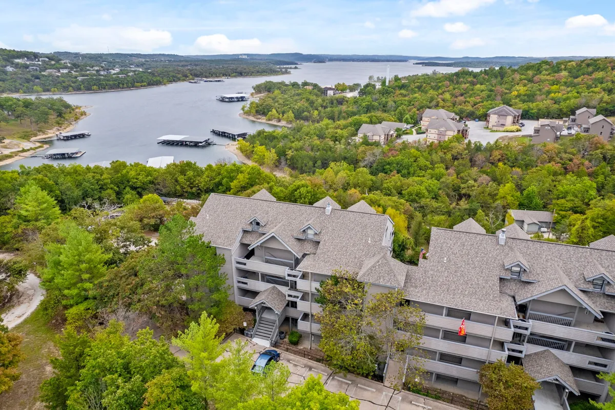 A tranquil lakeside scene featuring calm water, lush greenery, and resort buildings nestled among the trees. The view suggests opportunities for outdoor relaxation, birdwatching, or peaceful reflection by the water’s edge.