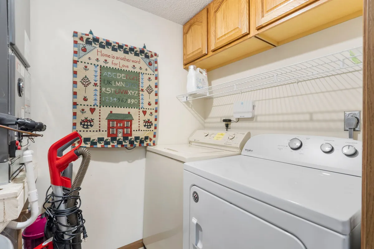 A tidy laundry area featuring a modern washing machine, a drying area for clothes, and a decorative quilt adding a personal touch. The space is organized and homey, emphasizing functionality and comfort.