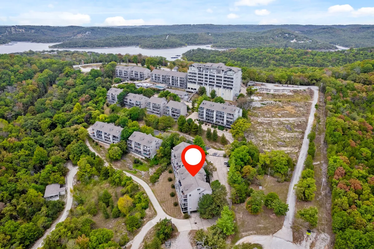 A broad exterior view capturing the cluster of condo buildings nestled among trees with a clear view of the lake. The atmosphere is calm and inviting, with visible nature paths and water, suggesting outdoor adventures and wildlife spotting just steps away from the residence.